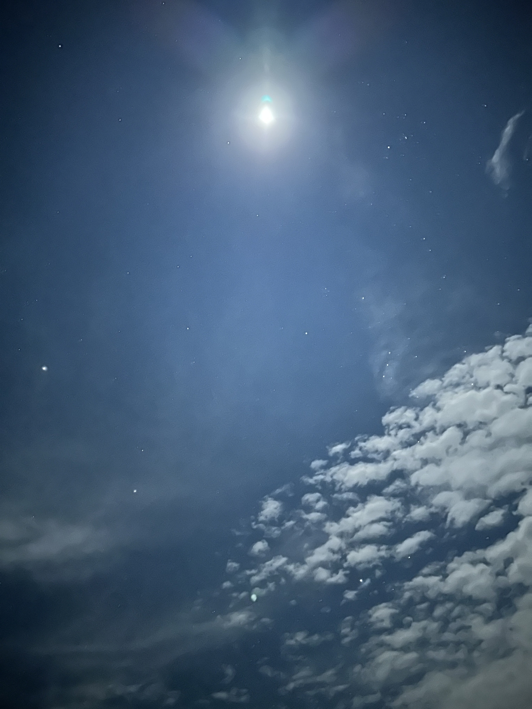 A bright moon illuminates a night sky with scattered stars and wispy clouds.