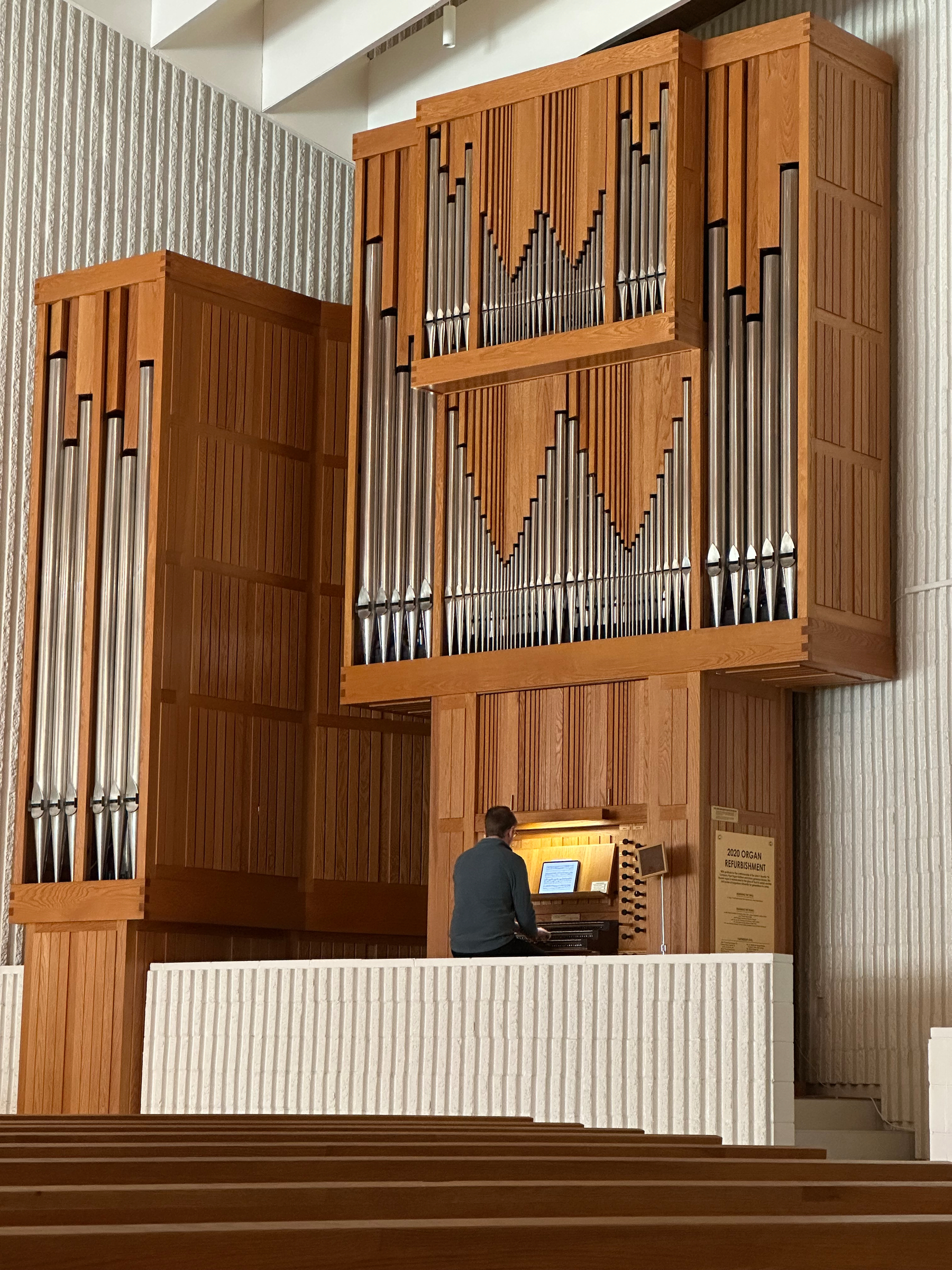 A person is playing a large wooden pipe organ inside a building with textured walls.