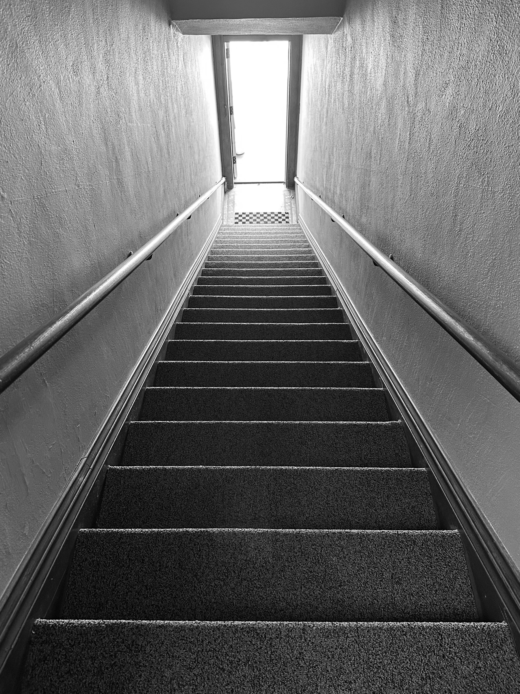 A staircase leads toward a bright, open doorway with walls on either side.