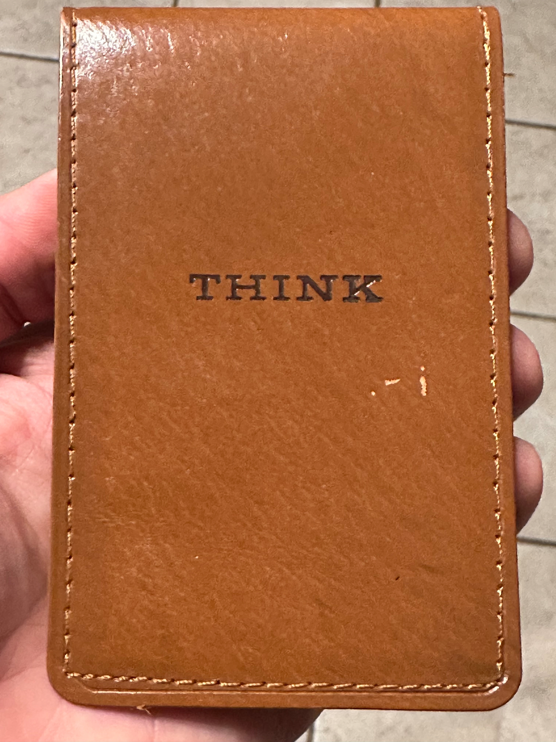 A hand is holding a brown leather notebook with the word THINK embossed on the cover.