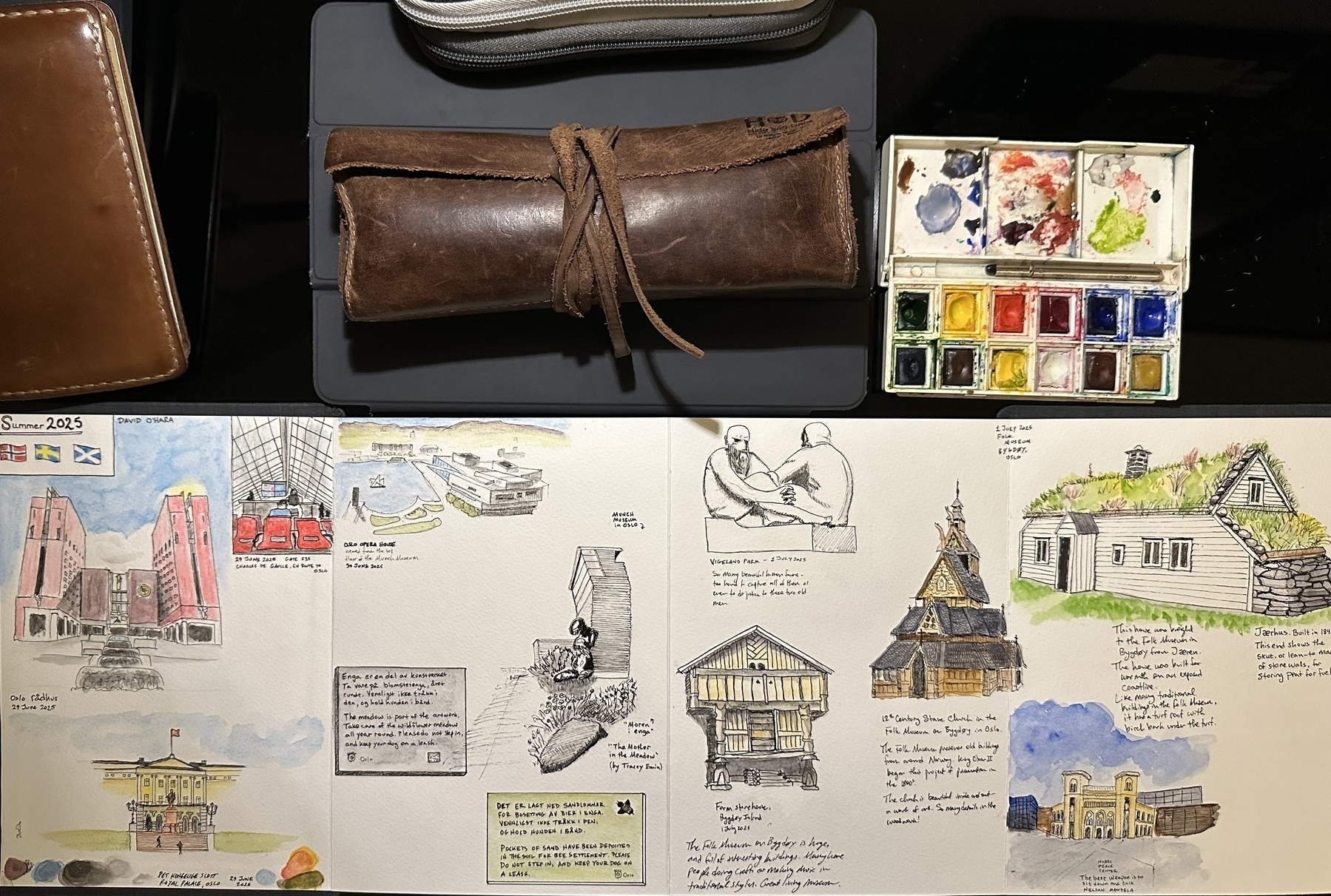 A collection of art supplies and a sketchbook showcasing various architectural drawings and sketches are displayed on a tabletop.
