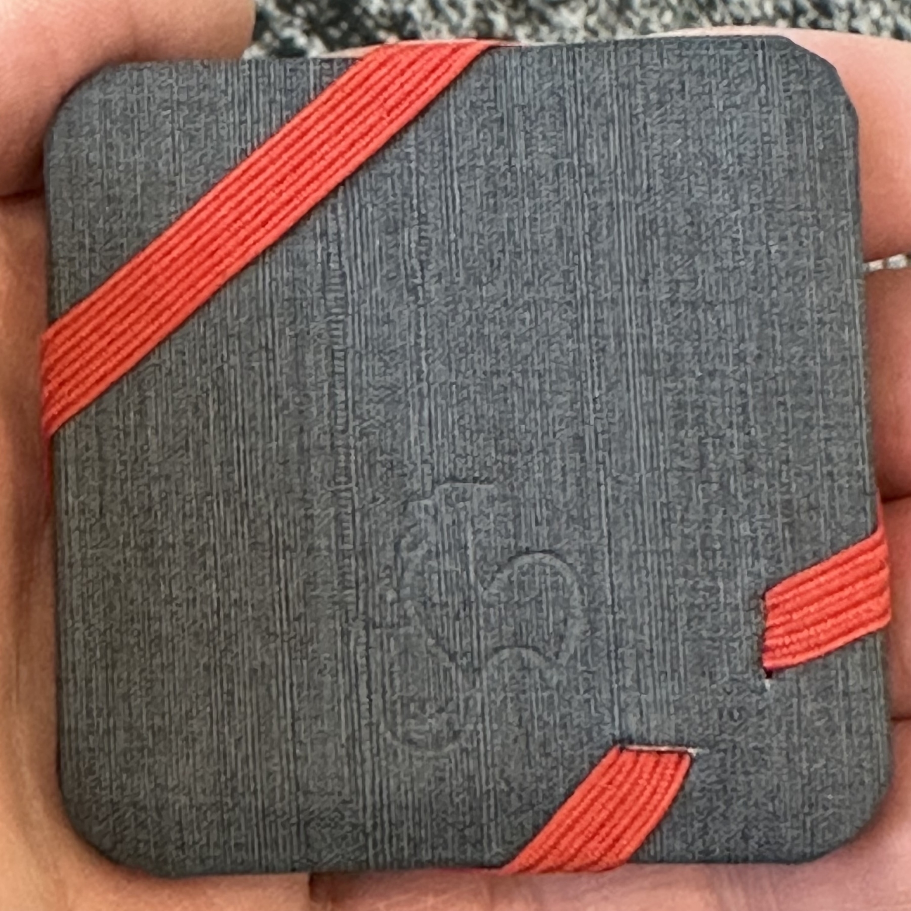 A hand is holding a textured square object wrapped with red elastic bands. The object is my pocket sketchbook. 