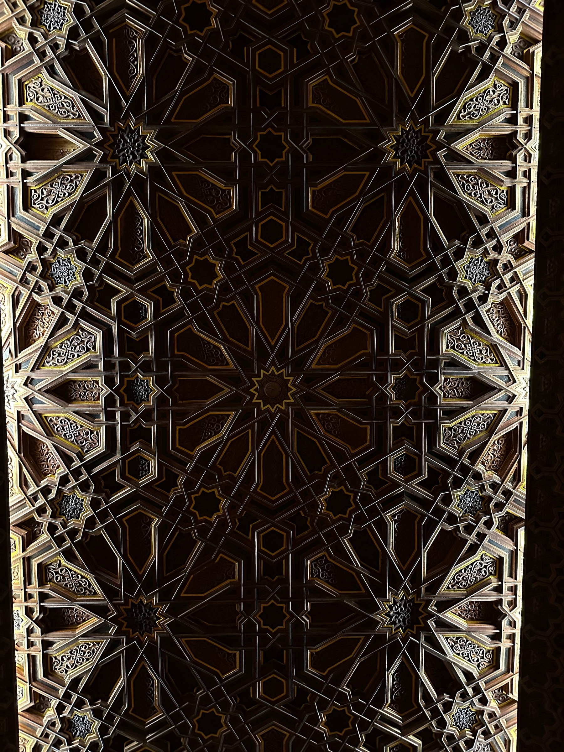 A detailed geometric pattern with intricate designs, featuring symmetrical star and floral motifs in a rich, dark color palette.