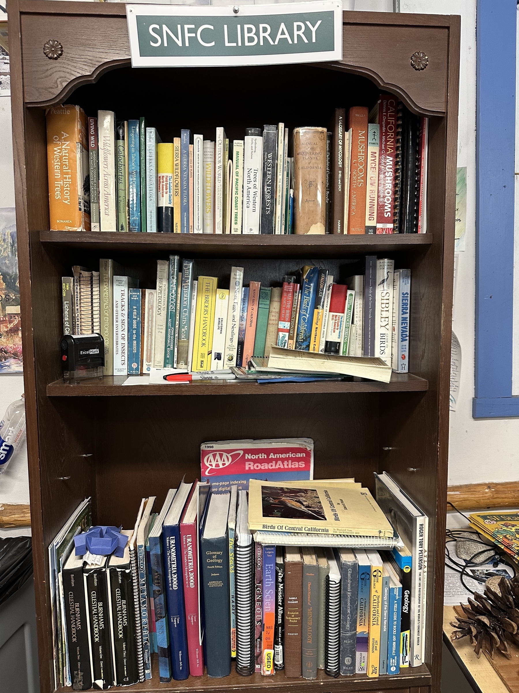 A rustic wooden bookshelf filled with well-worn nature field guides and maps