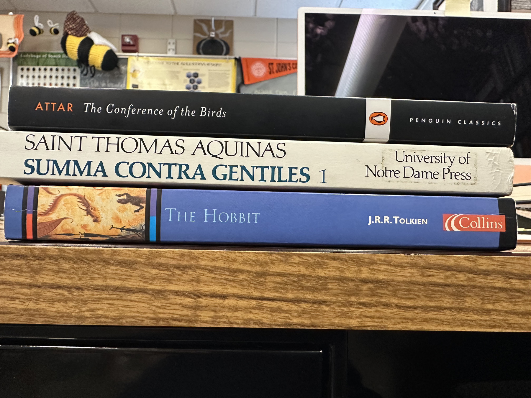 Three books stacked on a desk, including The Conference of the Birds, Thomas Aquinas' Summa Contra Gentiles I, and The Hobbit