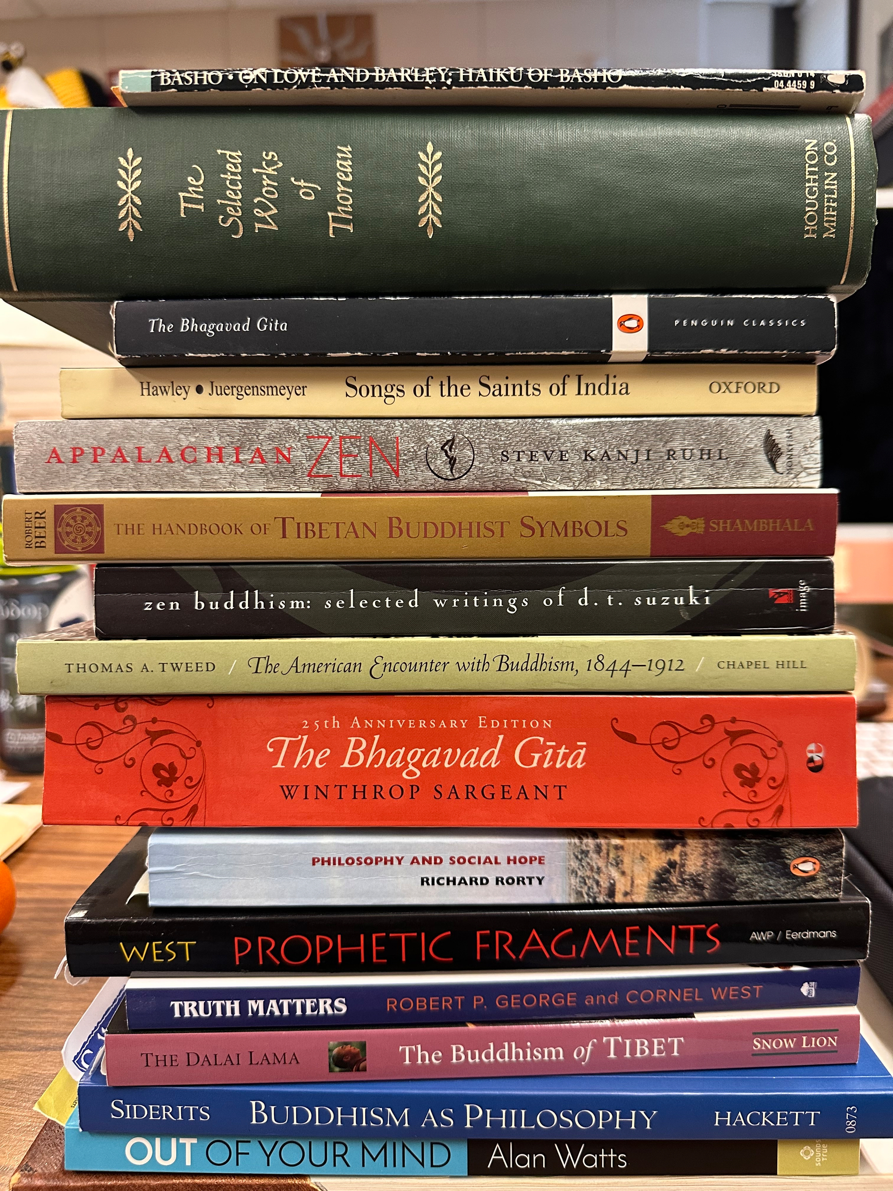A stack of diverse philosophy and religion books covering topics like Buddhism, Indian saints, and American transcendentalism.