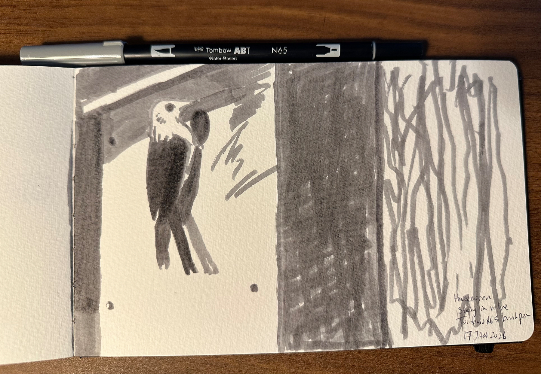 A black and white sketchbook drawing depicts a bird sitting on a birdhouse with abstract lines and shading, accompanied by a black pen on top.