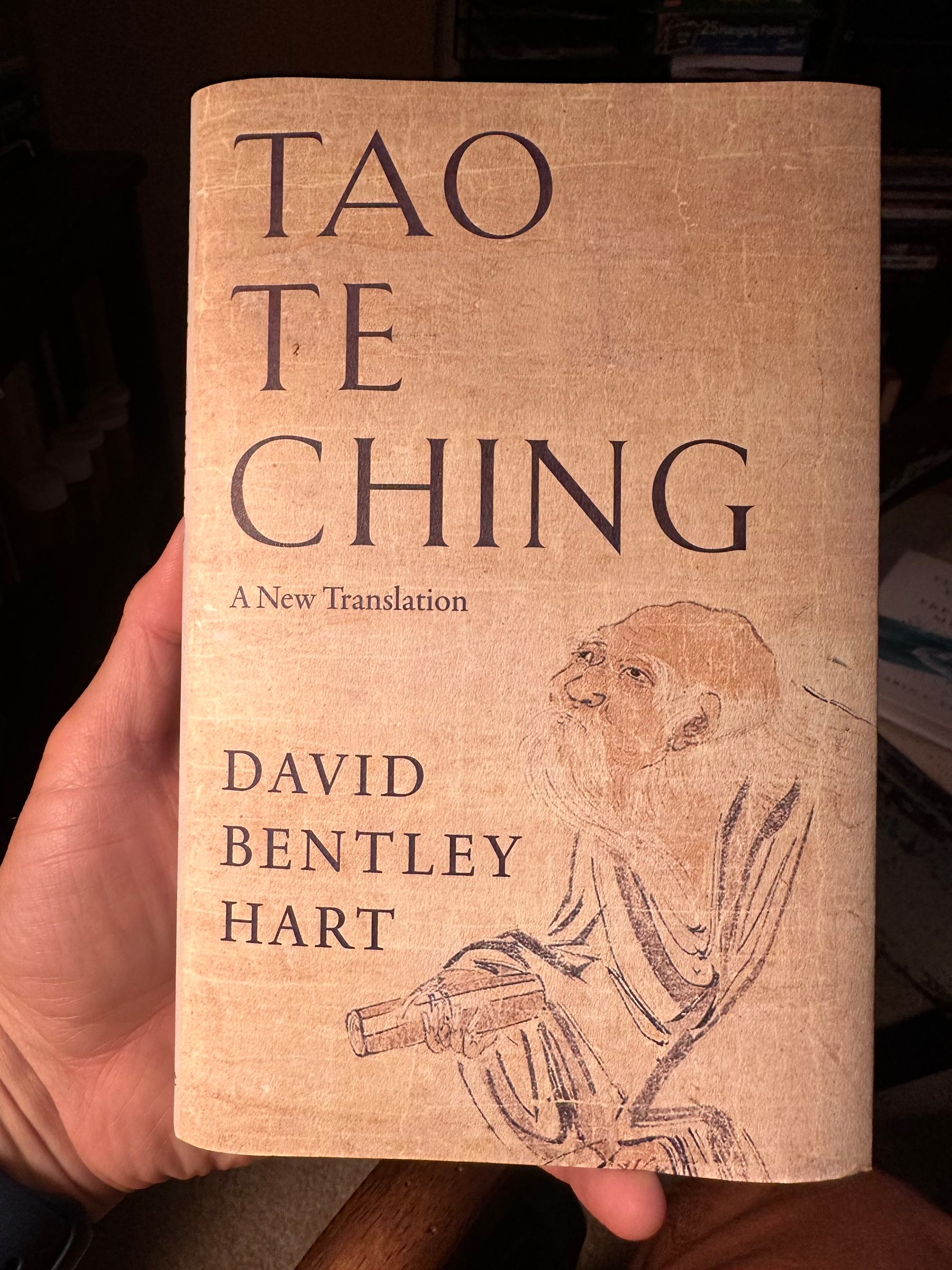 A hand is holding a book titled Tao Te Ching: A New Translation by David Bentley Hart, featuring an illustration of a bearded figure on the cover.