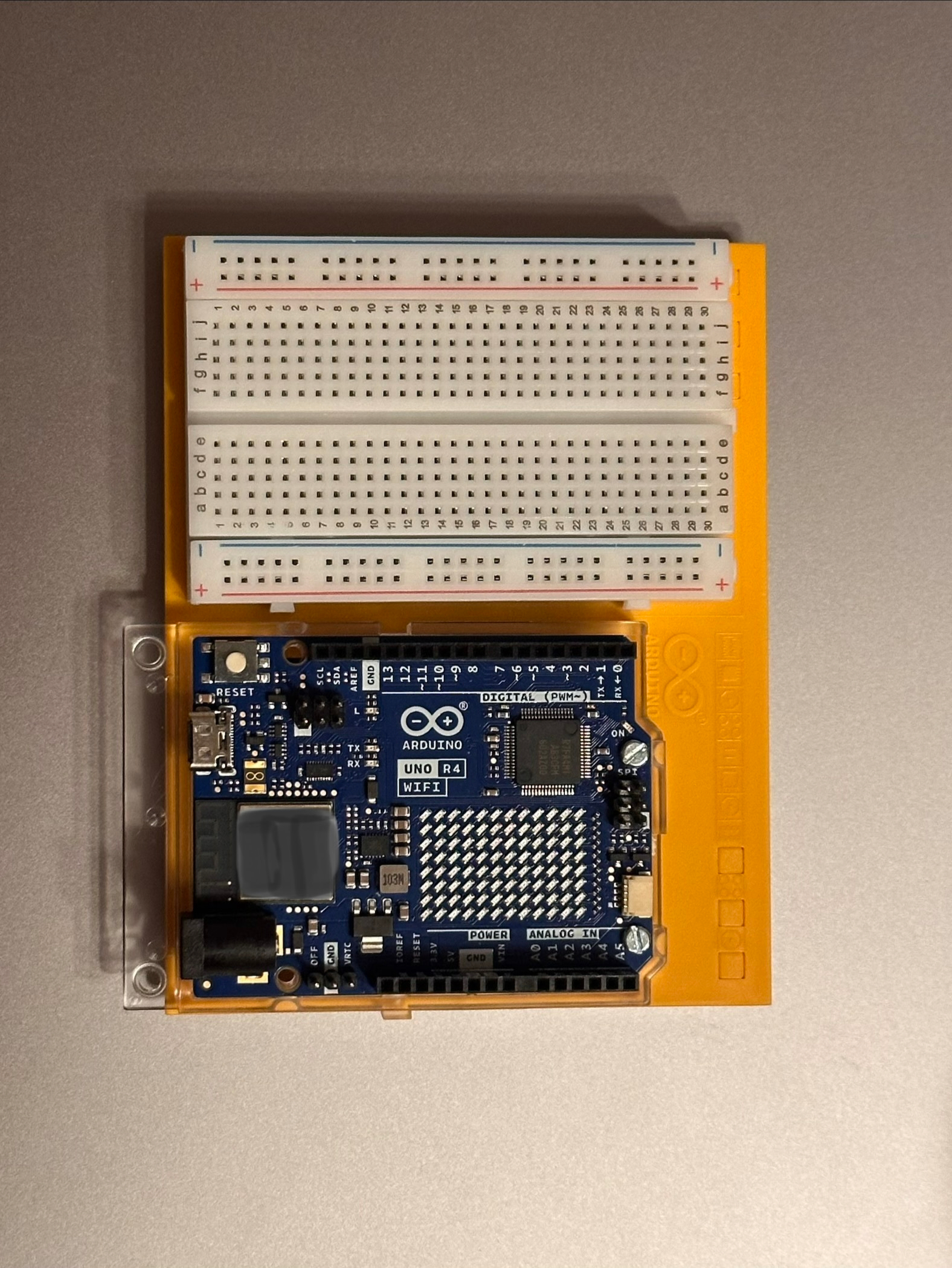 An Arduino Uno R4 WiFi microcontroller board is mounted on an orange base alongside a white solderless breadboard.