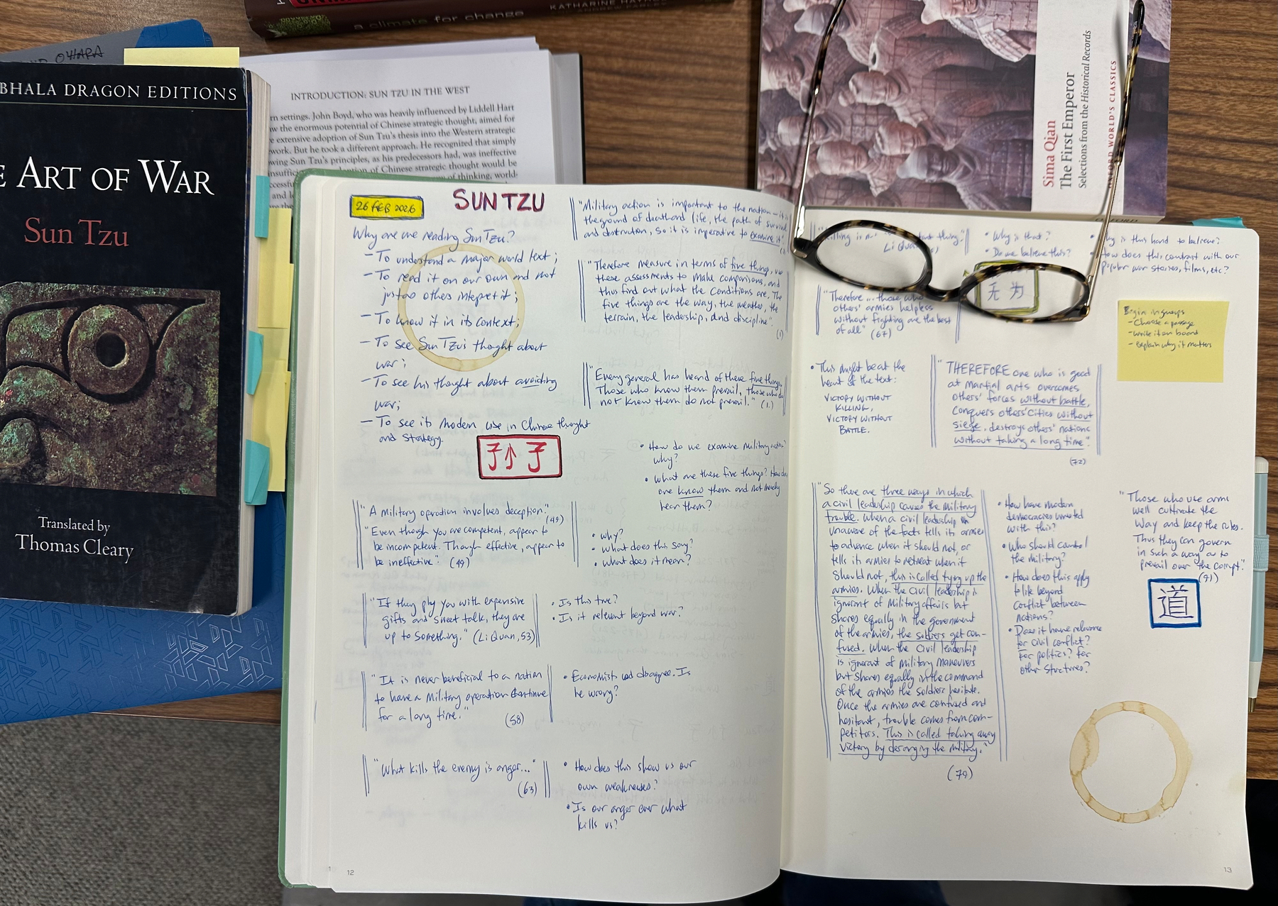 A journal filled with handwritten notes and glasses rests on an open page, surrounded by books including The Art of War by Sun Tzu.