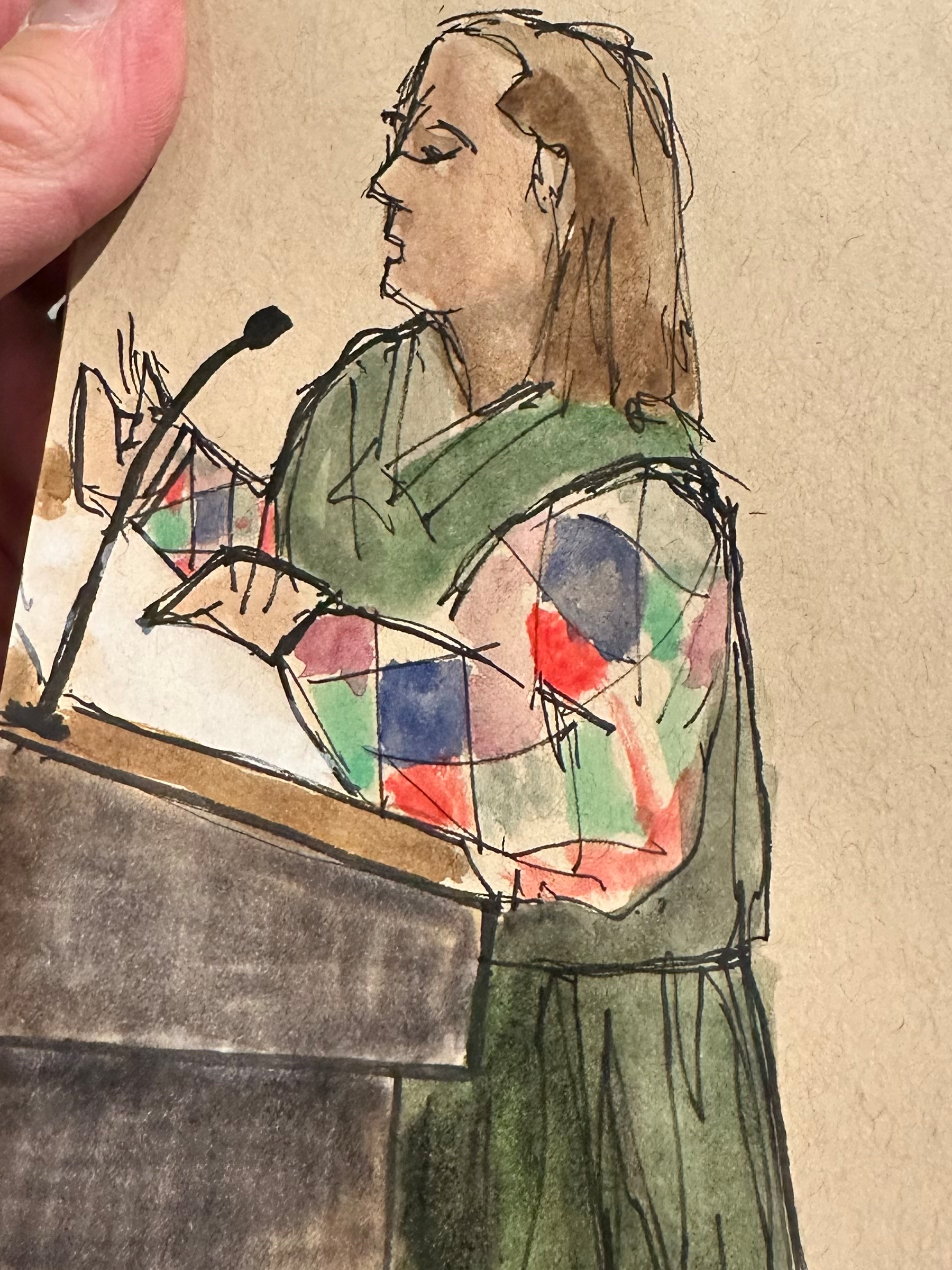 A person wearing a colorful checkered shirt and a green vest is standing at a podium, speaking into a microphone.
