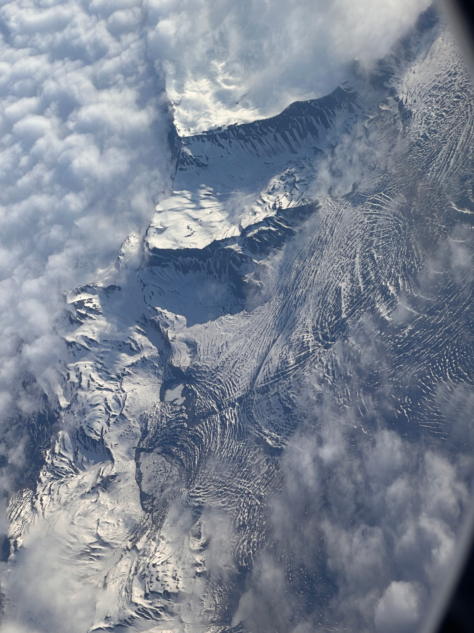 Snow-covered mountain peaks and glaciers are partially obscured by surrounding clouds.