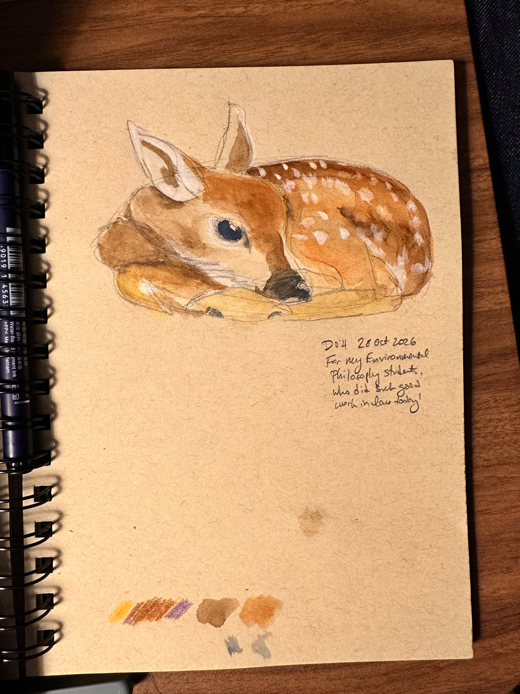 A watercolor painting of a fawn lying down is depicted on a sketchbook page, accompanied by handwritten notes and color swatches.
